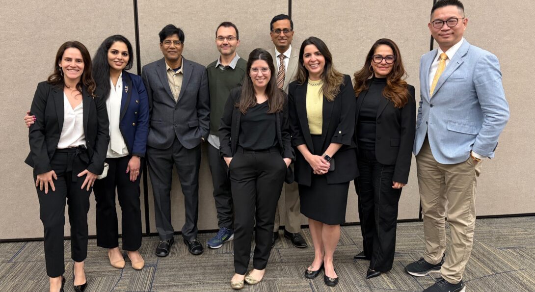 Nine Hatton Award Committee members professionally dressed standing together, smiling warmly. They convey a sense of teamwork and approachability against a plain backdrop at the 2026 AADOCR/IADR Conference.