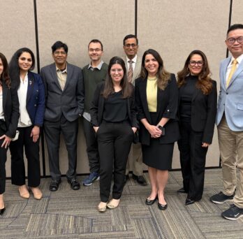 Nine Hatton Award Committee members professionally dressed standing together, smiling warmly. They convey a sense of teamwork and approachability against a plain backdrop at the 2026 AADOCR/IADR Conference. 